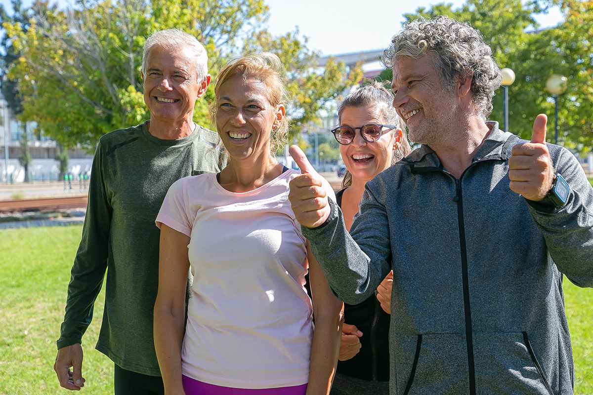 happy excited sporty mature people standing together after morning exercises park looking away smiling making thumb up gesture retirement active lifestyle concept